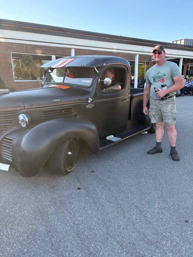 Two visitors beside a matte black Dodge pickup at the car show