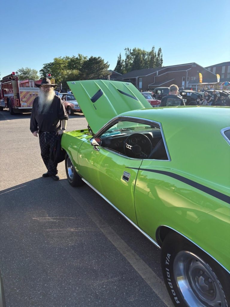A visitor beside a lime green Plymouth Barracuda with the hood up