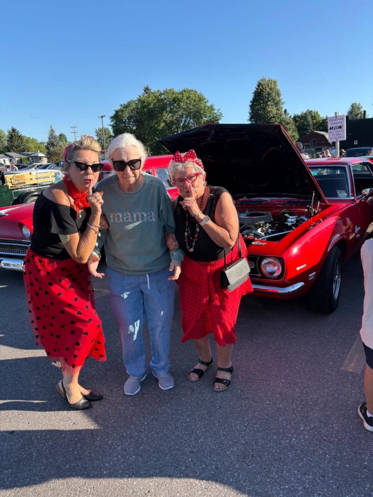 Three guests in nineteen-fifties dress posing in front of a red Camaro