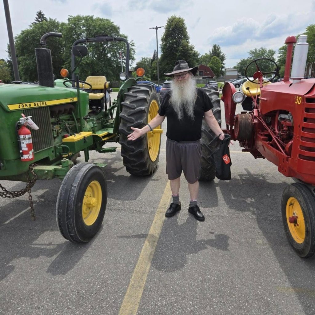A Pioneer and Hobby Club member between a green John Deere and a red Massey Harris 30