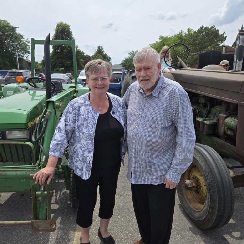 A couple from the Pioneer and Hobby Club beside their John Deere tractors